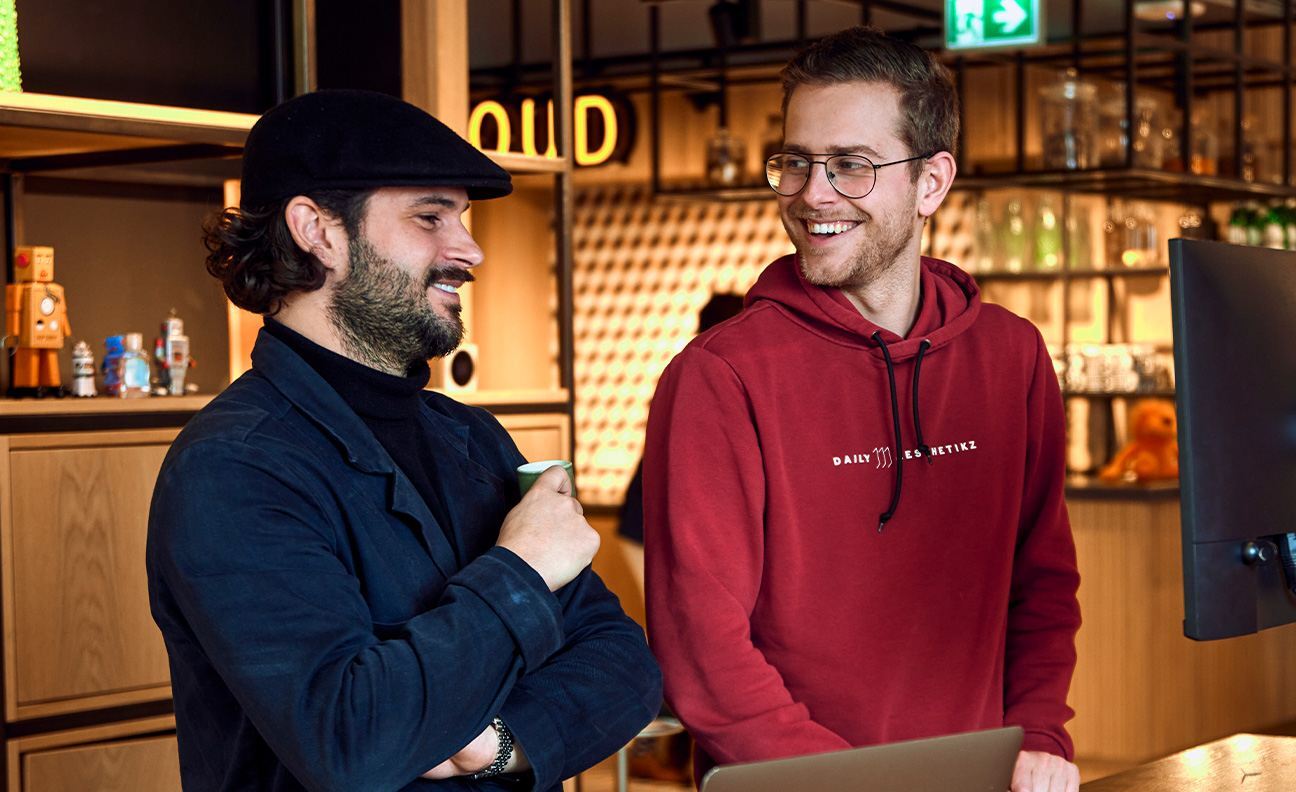 twee jonge mannen lachen naar elkaar achter laptop