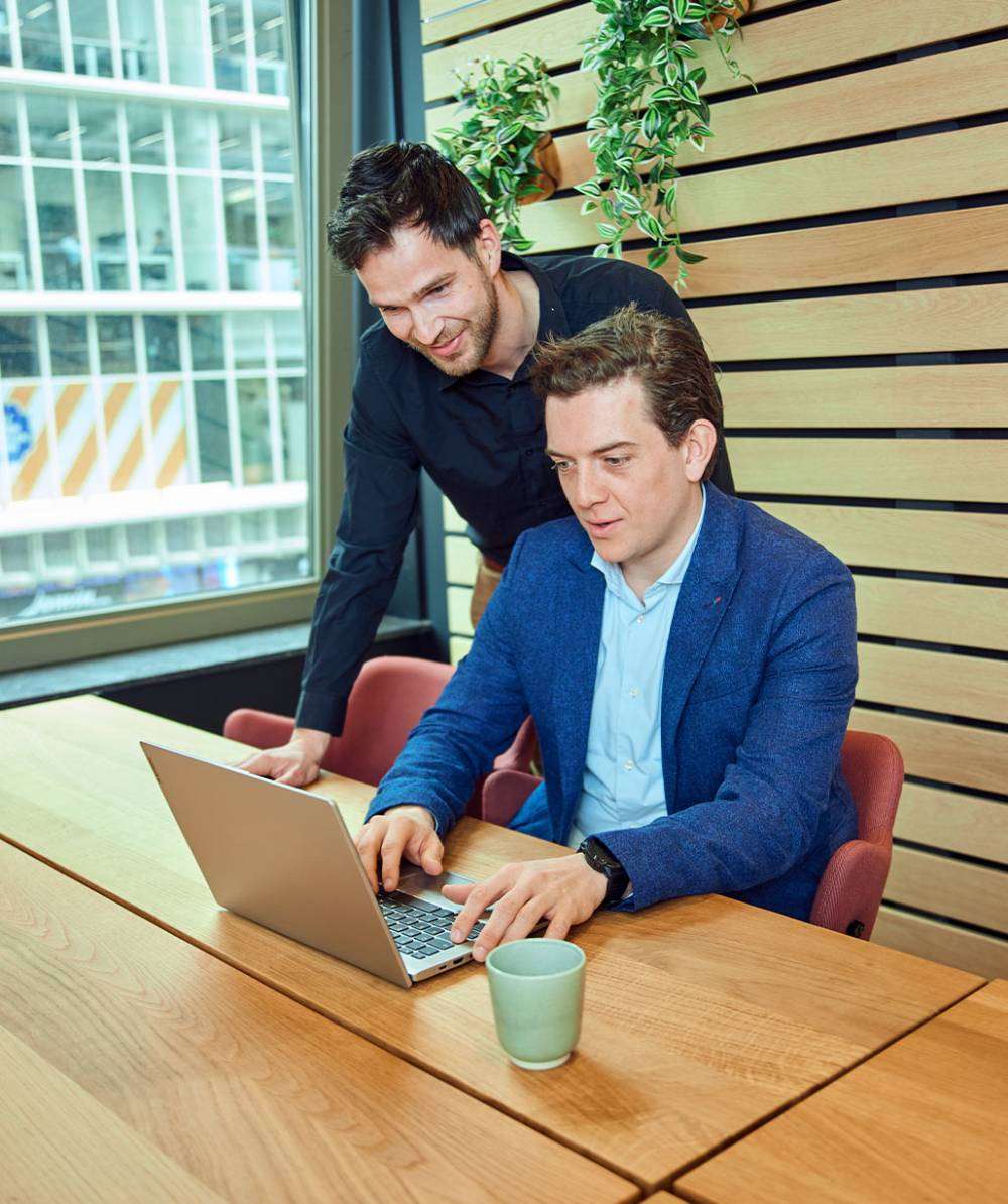 Werknemers kijken samen naar laptop op kantoor.