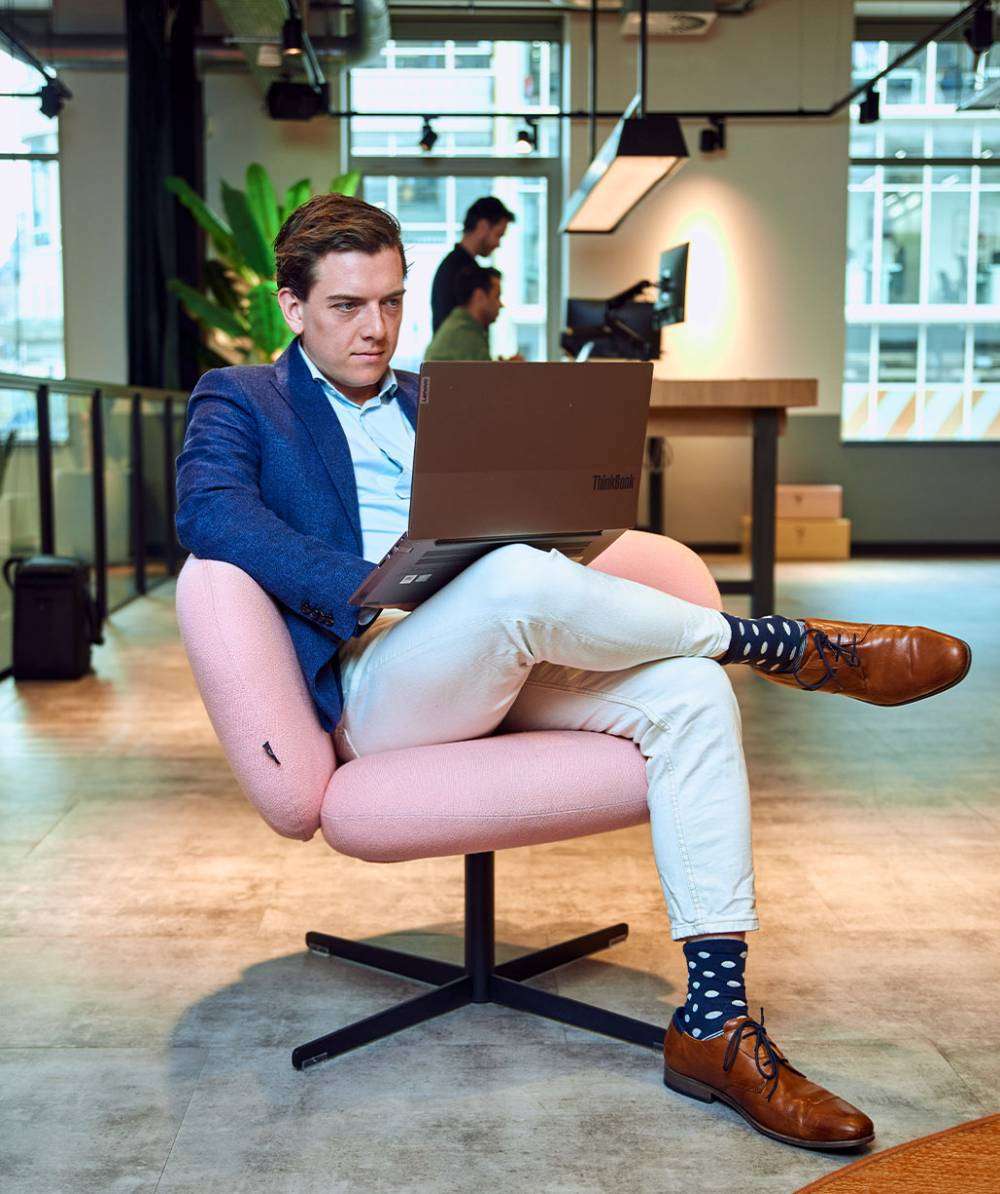 man-uitgezoomd-roze-stoel-werken-laptop