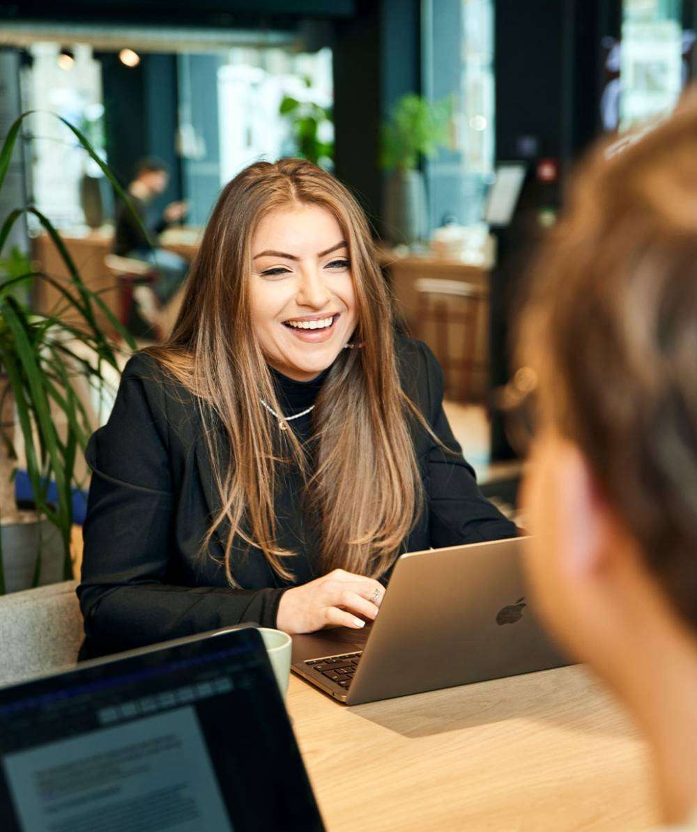 Vrouw achter laptop lachend naar collega.